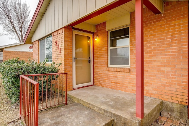 view of exterior entry featuring board and batten siding and brick siding