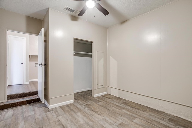 unfurnished bedroom featuring ceiling fan, a textured ceiling, light wood-style flooring, visible vents, and a closet