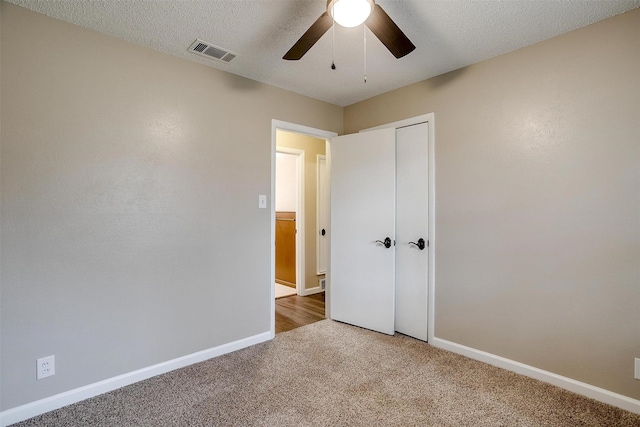 unfurnished bedroom with a textured ceiling, carpet flooring, visible vents, baseboards, and a closet