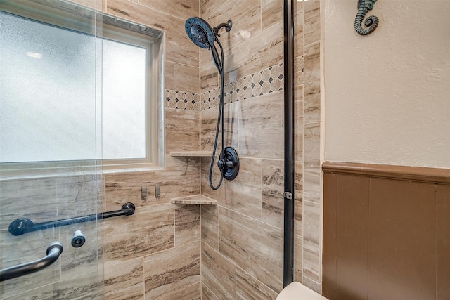 bathroom with wainscoting and a tile shower