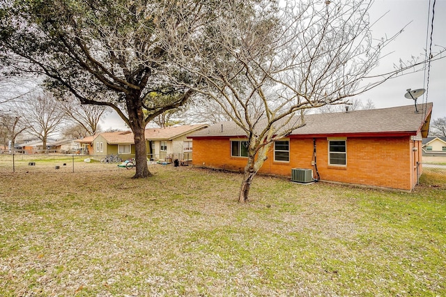 rear view of property featuring a yard, cooling unit, brick siding, and fence