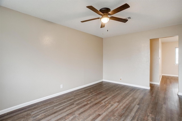 empty room with dark wood-style floors, a ceiling fan, visible vents, and baseboards