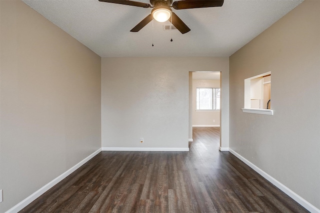 spare room with a ceiling fan, visible vents, dark wood finished floors, and baseboards