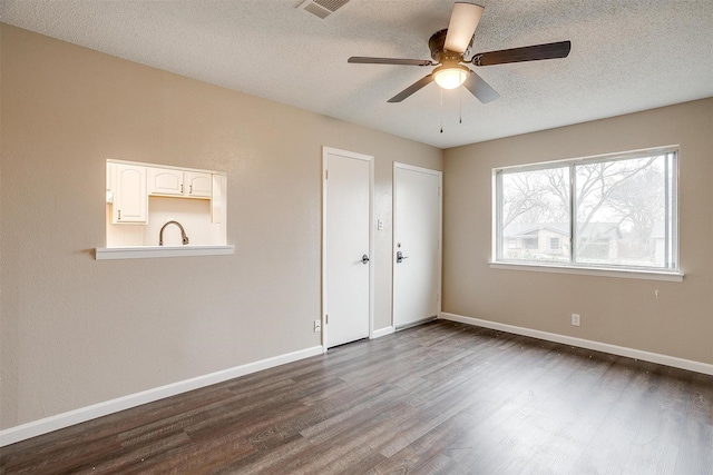 empty room with dark wood-style flooring, visible vents, a sink, a textured ceiling, and baseboards