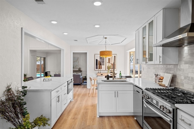 kitchen featuring appliances with stainless steel finishes, white cabinets, glass insert cabinets, and wall chimney exhaust hood