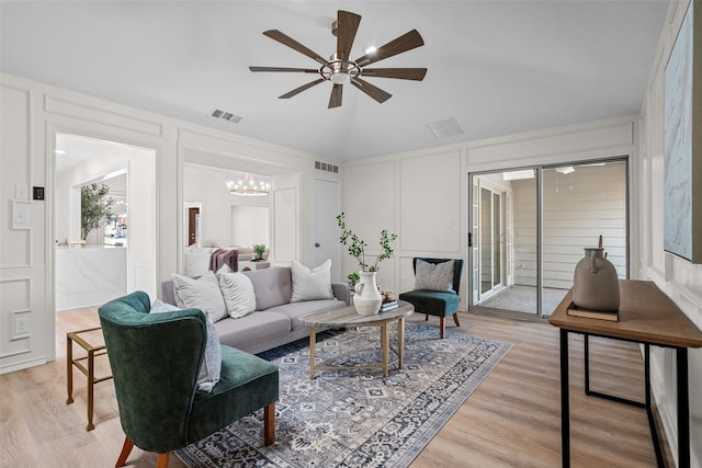 living area featuring vaulted ceiling, light wood-style flooring, visible vents, and a decorative wall