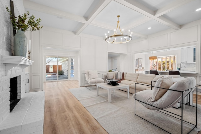 living room with a wealth of natural light, a decorative wall, light wood-style floors, a brick fireplace, and coffered ceiling