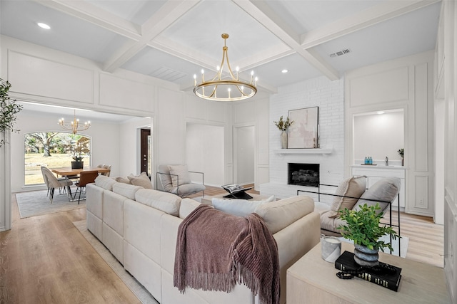 living area featuring an inviting chandelier, light wood-style flooring, visible vents, and coffered ceiling