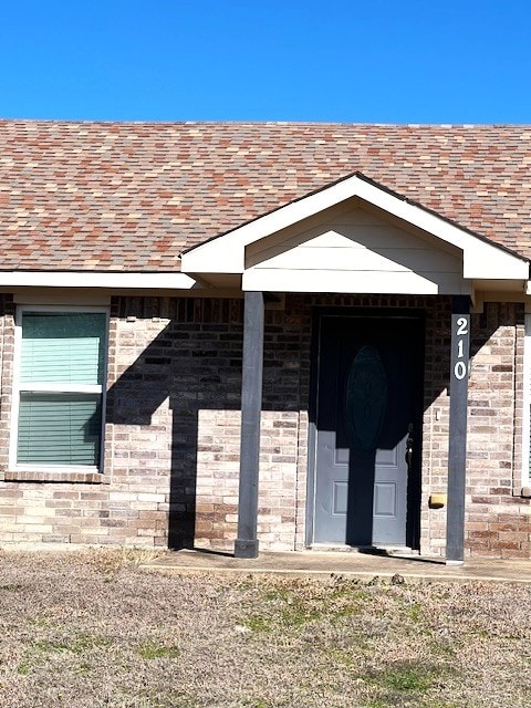 property entrance with a shingled roof and brick siding