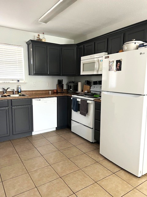 kitchen featuring light tile patterned floors, dark countertops, a sink, dark cabinets, and white appliances