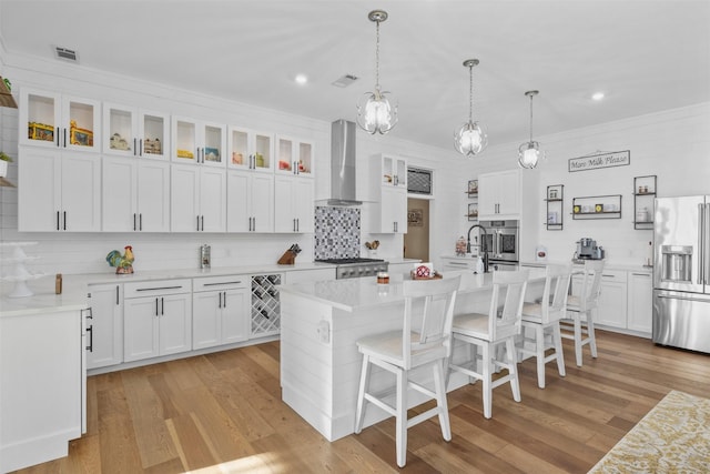 kitchen with white cabinets, light countertops, appliances with stainless steel finishes, wall chimney exhaust hood, and glass insert cabinets