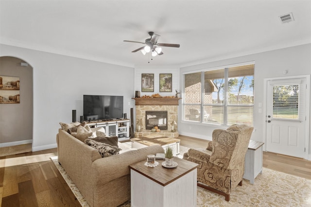 living area with arched walkways, light wood-style flooring, a fireplace, visible vents, and baseboards