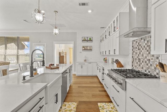 kitchen with wall chimney range hood, appliances with stainless steel finishes, glass insert cabinets, and white cabinetry