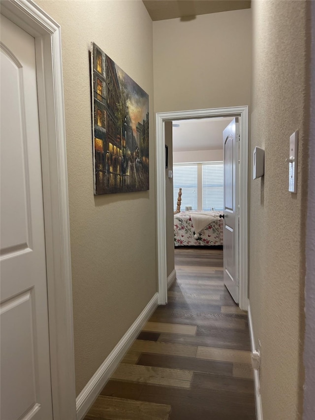 hall featuring dark wood-style flooring, a textured wall, and baseboards