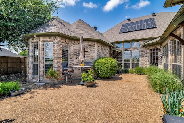 rear view of house featuring roof with shingles, fence, solar panels, and brick siding