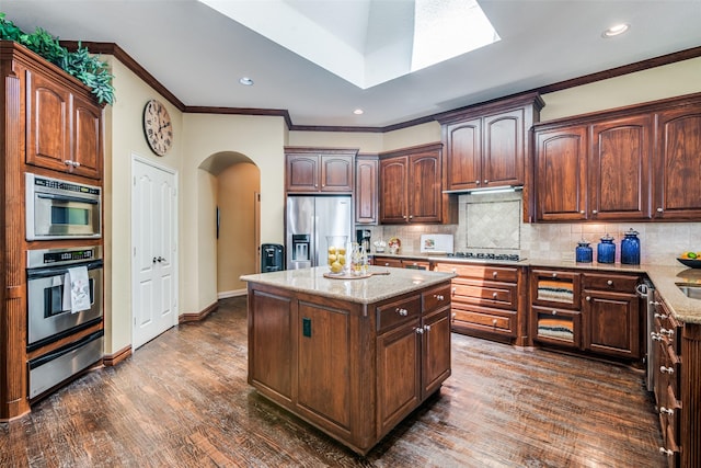 kitchen with arched walkways, stainless steel appliances, a center island, decorative backsplash, and a warming drawer