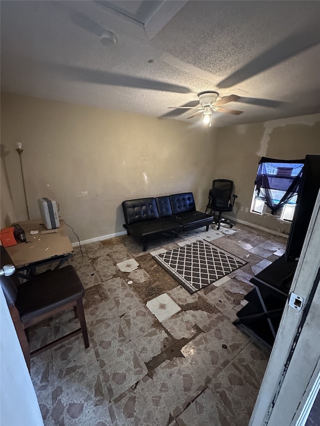 living room with ceiling fan, a textured ceiling, and baseboards