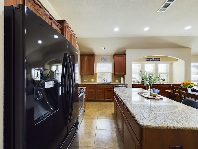 kitchen featuring a kitchen island, a healthy amount of sunlight, black refrigerator with ice dispenser, and tasteful backsplash