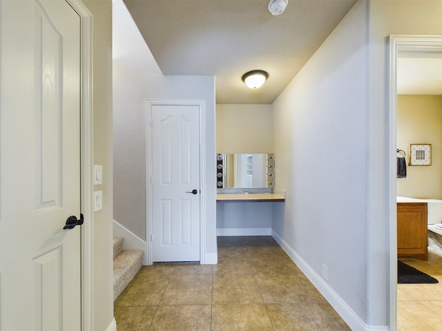 corridor featuring stairs, baseboards, and light tile patterned flooring