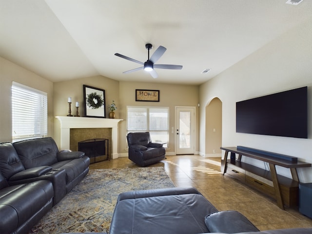 tiled living area featuring arched walkways, a fireplace, lofted ceiling, visible vents, and baseboards