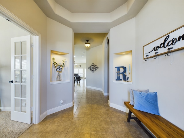 hallway with light tile patterned floors, a tray ceiling, and baseboards