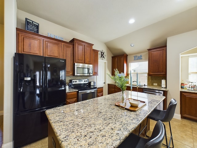 kitchen featuring stainless steel appliances, a center island, a breakfast bar, and light stone counters