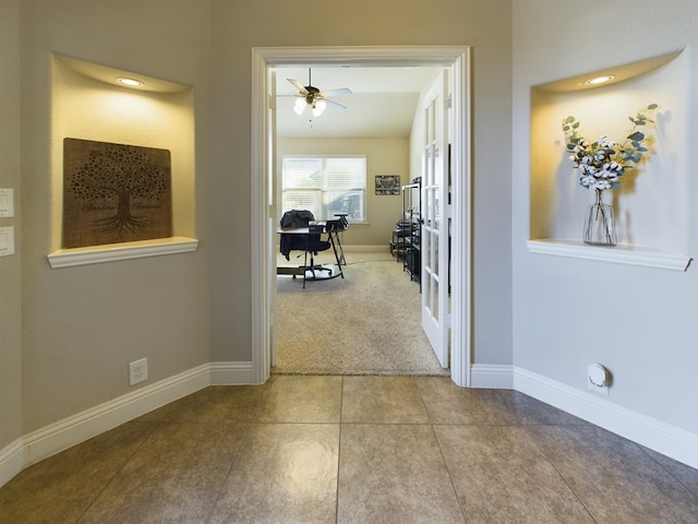 hallway with light carpet, light tile patterned floors, and baseboards