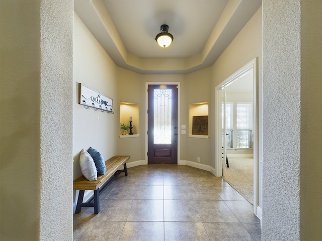 foyer with light tile patterned floors, a tray ceiling, and baseboards