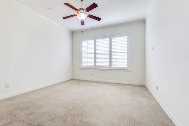 empty room with ornamental molding, light colored carpet, ceiling fan, and baseboards