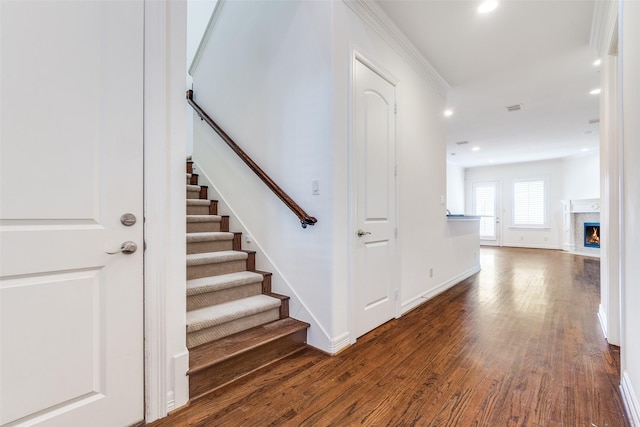 stairway featuring visible vents, baseboards, a fireplace with flush hearth, wood finished floors, and recessed lighting