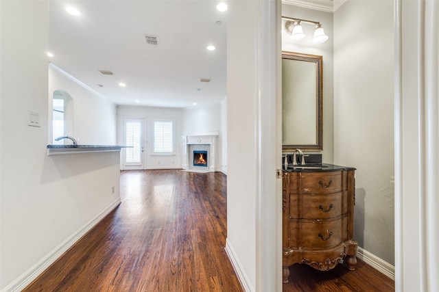 corridor with a sink, wood finished floors, visible vents, and baseboards