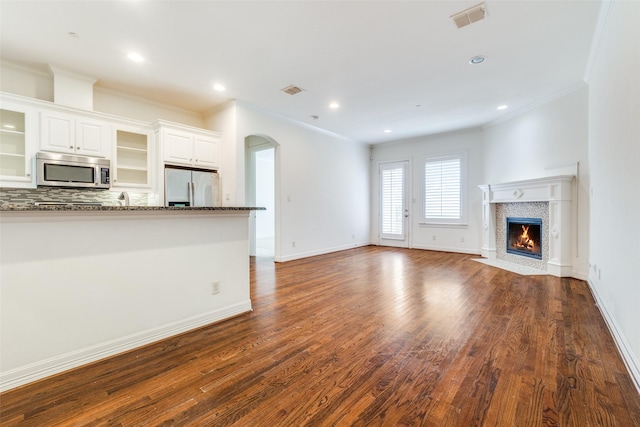 unfurnished living room with dark wood-type flooring, a fireplace with flush hearth, visible vents, baseboards, and ornamental molding