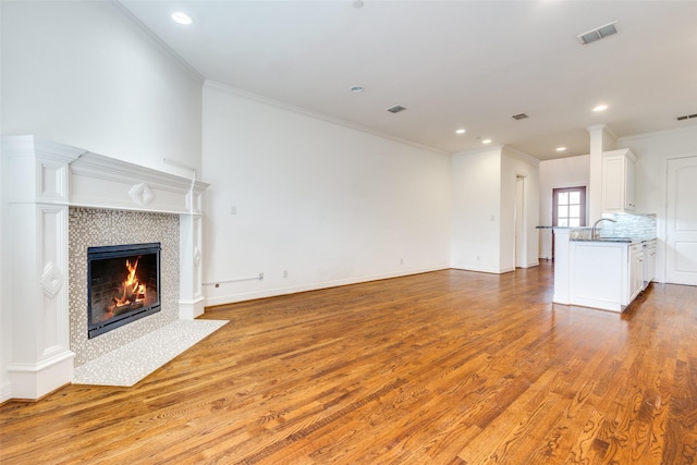 unfurnished living room featuring light wood finished floors, visible vents, crown molding, a fireplace, and a sink