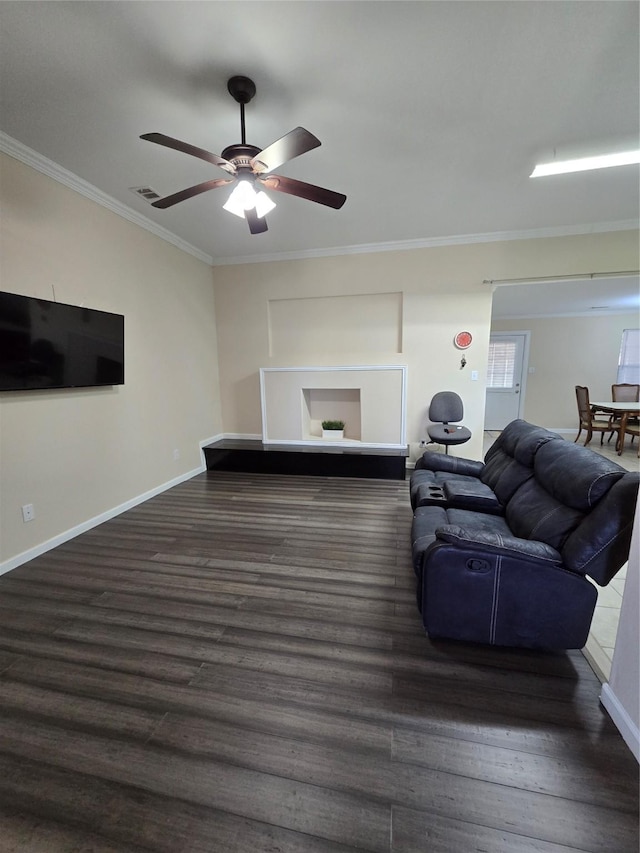 living room featuring a ceiling fan, visible vents, baseboards, ornamental molding, and dark wood finished floors