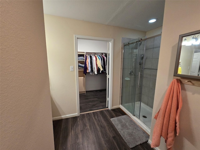 full bathroom with a walk in closet, a shower stall, baseboards, and wood finished floors