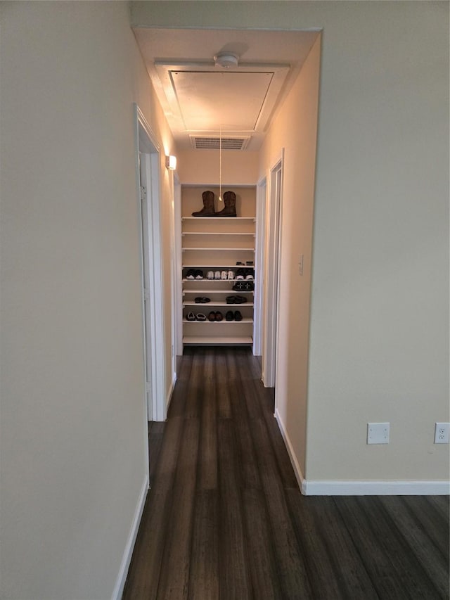 hallway featuring attic access, built in shelves, baseboards, and dark wood-style flooring