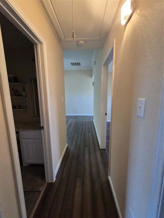 corridor featuring attic access, visible vents, baseboards, and dark wood-style floors