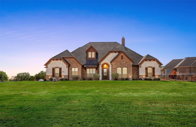 french country home featuring brick siding, a lawn, a chimney, and roof with shingles