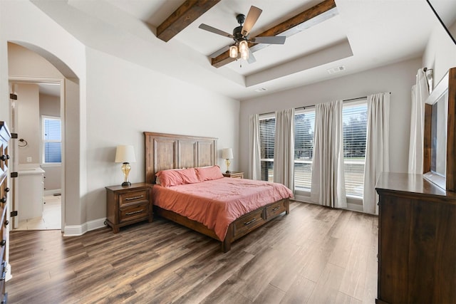 bedroom featuring baseboards, arched walkways, wood finished floors, a tray ceiling, and beam ceiling