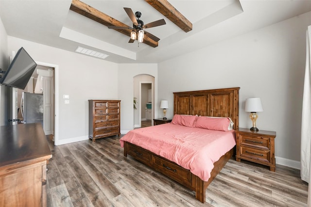 bedroom with a tray ceiling, arched walkways, visible vents, wood finished floors, and baseboards