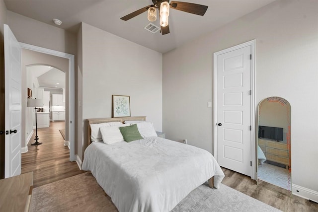 bedroom with arched walkways, visible vents, baseboards, and wood finished floors