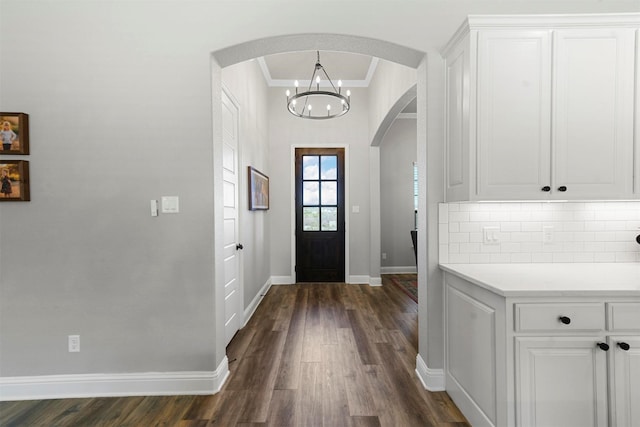 entryway featuring ornamental molding, arched walkways, dark wood finished floors, and baseboards