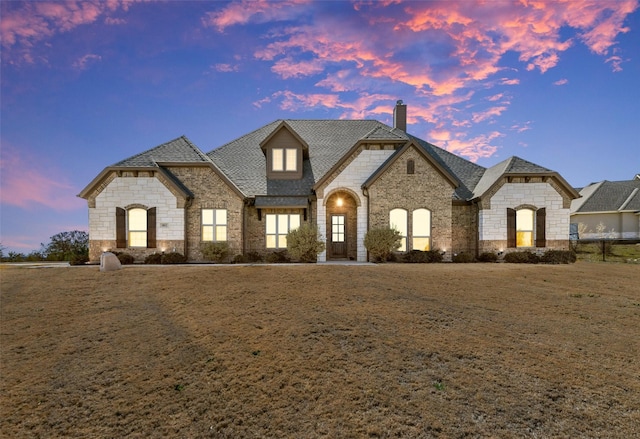 french country style house with brick siding, a chimney, and roof with shingles