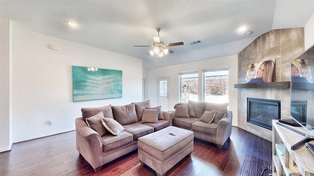 living area with dark wood-style floors, vaulted ceiling, a tile fireplace, and visible vents