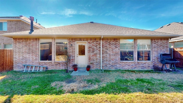 rear view of house featuring brick siding, a lawn, and roof with shingles