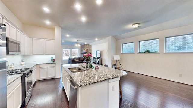 kitchen with light stone counters, stainless steel appliances, open floor plan, white cabinets, and an island with sink