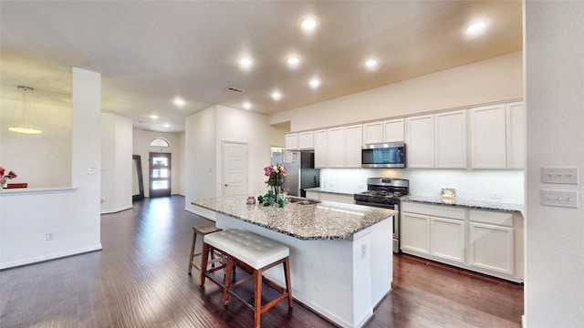 kitchen featuring white cabinets, appliances with stainless steel finishes, light stone counters, a kitchen breakfast bar, and a kitchen island with sink