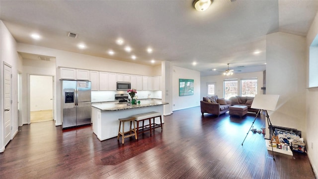 kitchen featuring stainless steel appliances, open floor plan, white cabinets, a kitchen island, and dark stone counters