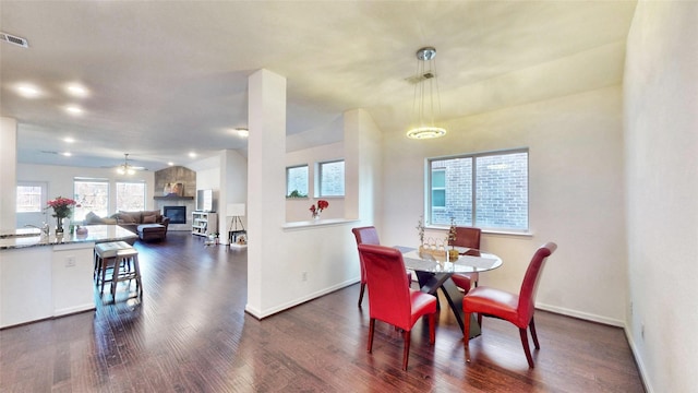 dining room featuring dark wood-type flooring, visible vents, a ceiling fan, baseboards, and a glass covered fireplace