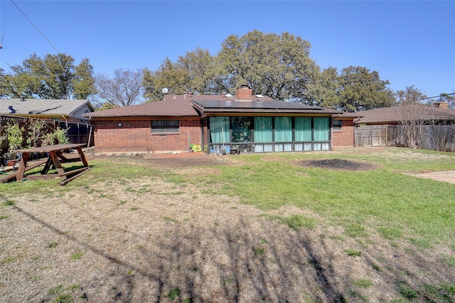 rear view of property featuring roof mounted solar panels, brick siding, a lawn, and fence